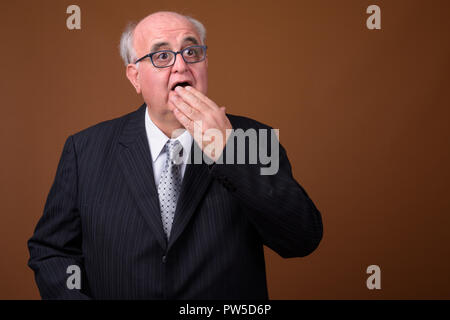 L'embonpoint senior businessman wearing eyeglasses contre brown b Banque D'Images