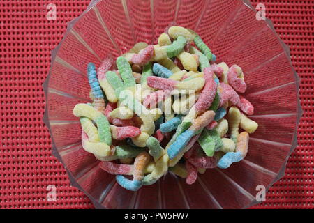 Close-up of gummy worm de bonbons dans un bol en plastique sur une table orange Banque D'Images