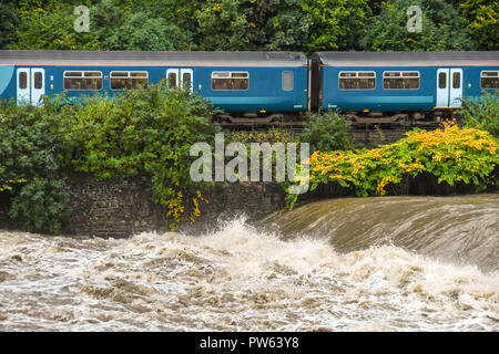 RADYR, près de Cardiff, Pays de Galles - 13 octobre 2018 : le dernier jour de l'exécution de ses 15 ans au Pays de Galles et le rail, une franchise frontières Arriva Trains Wales commuter train passe la forte montée des eaux sur la rivière Taff au Radyr weir près de Cardiff. Le niveau d'eau extrêmement élevé est le résultat de la tempête Callum. La rivière Taff, qui se jette dans le canal de Bristol à Cardiff Bay, draine l'eau de la montagne Brecon Beacons et la Galles du sud des vallées. Credit : Ceri/Alamy Breeze Live News Banque D'Images