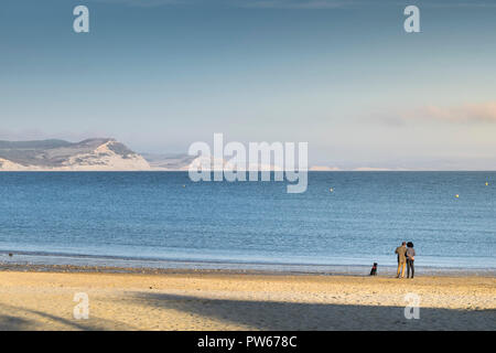 Un couple et leur chien sur la plage de Lyme profitant de la lumière du soir à la ville côtière de Lyme Regis dans le Dorset. Banque D'Images