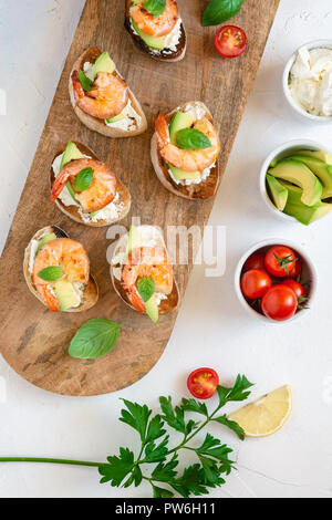 Snack-sandwiches italiens Bruschetta aux crevettes, avocat et fromage décoré par le basilic. Banque D'Images