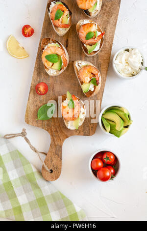 Snack-sandwiches italiens Bruschetta aux crevettes, avocat et fromage décoré par le basilic. Banque D'Images