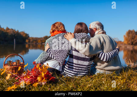 Les parents de détente au lac d'automne avec leur fille adulte. Les valeurs familiales. Les gens prenant le thé et s'étreindre Banque D'Images
