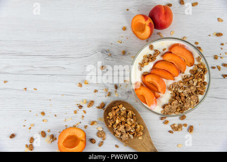 Un bol rempli de yaourt à l'abricot et une cuillère en bois plein de muesli sur une table en bois blanc, vue du dessus, copy space Banque D'Images