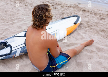 Bel homme est assis sur la plage avec un voile blanc vide attendre Vague à surf en mer ocean shore. Concept de sport, fitness, liberté, bonheur, nouvelle vie moderne, hipster. Banque D'Images