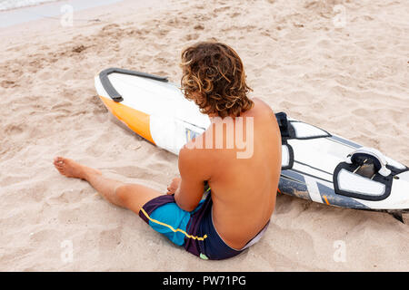 Bel homme est assis sur la plage avec un voile blanc vide attendre Vague à surf en mer ocean shore. Concept de sport, fitness, liberté, bonheur, nouvelle vie moderne, hipster. Banque D'Images