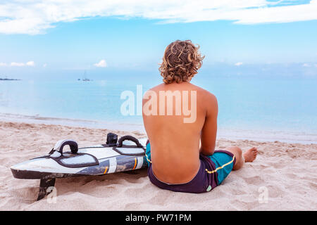 Bel homme est assis sur la plage avec un voile blanc vide attendre Vague à surf en mer ocean shore. Concept de sport, fitness, liberté, bonheur, nouvelle vie moderne, hipster. Banque D'Images