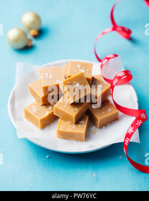 Fudge au caramel bonbons frais sur une plaque avec du ruban rouge de Noël sur fond bleu Banque D'Images