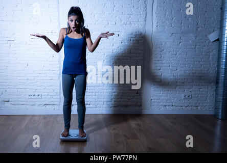 Jeune femme slim fit et contrôle de poids du corps sur l'échelle se trouvant en gras et se sentir déprimé et désespéré avec grande lumière ombre edgy en mangeant di Banque D'Images