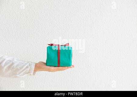 Young caucasian woman tient dans la main boîte-cadeau enveloppé dans du papier vert attaché avec un ruban rouge. Arrière-plan blanc. Nouvel An Noël Saint Valentin anniversaire pre Banque D'Images