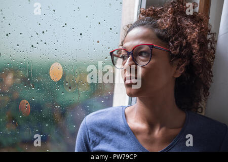 Triste african american girl en regardant par la fenêtre de temps de pluie