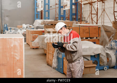 Le magasinier marque l'arrivée sur la tablette. homme conduisant un chariot élévateur dans un entrepôt d'une usine pilote. en uniforme et casque de protection. Le concept de logistique et stockage Banque D'Images