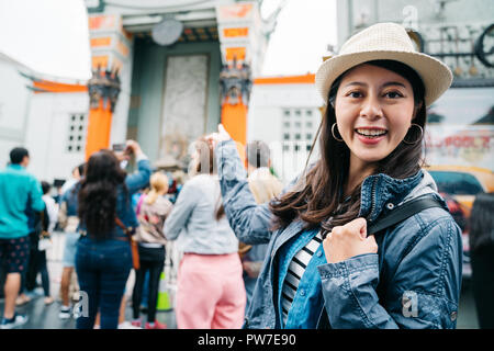 Female traveler in et excité pointant vers le théâtre chinois. jeune voyageur face à l'appareil photo en souriant. Backpacker asiatique montrant la fam Banque D'Images