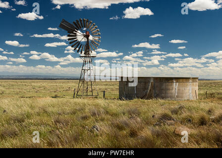 Vintage outback australien moulin pompe à eau et réservoir en béton sur une journée ensoleillée avec des nuages gonflés. Banque D'Images