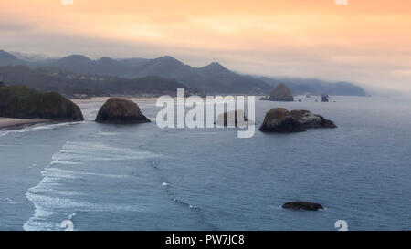 Côte du Pacifique. Vue du parc d'état d'Ecola. Des roches et des pierres dans l'eau avec Haystack Rock près de Cannon Beach. Éclaboussures des vagues à marée haute. Banque D'Images