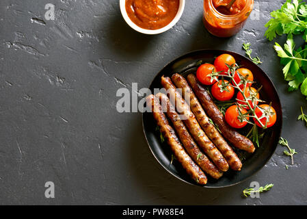 Saucisses frites et les tomates cerise sur plaque sur fond noir en noir avec l'exemplaire de l'espace. Haut de la vue, télévision lay Banque D'Images