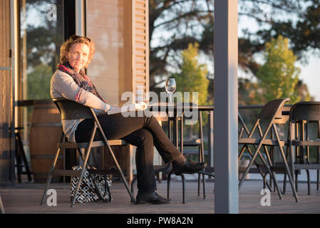 Une femme lisant un livre avec un verre de vin blanc sur une table à côté d'elle en après-midi au soleil Rowlee Winery près d'Orange dans l'ouest de la Nouvelle-Galles du Sud Banque D'Images