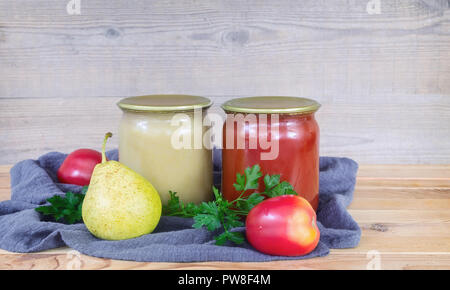 Purée de poire et le jus de tomate sont conservés dans des bocaux en verre avec couvercles métalliques scellés. Près de se coucher les poires et les tomates. Banque D'Images