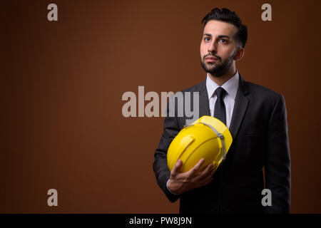 Beau jeune homme d'affaires iranien barbu avec un casque de protection contre Banque D'Images