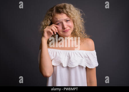 Belle jeune femme aux cheveux bouclés blonds contre gray background Banque D'Images