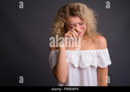 Belle jeune femme aux cheveux bouclés blonds contre gray background Banque D'Images