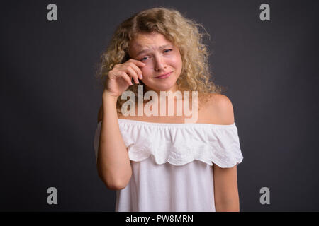 Studio shot of young Beautiful woman with blonde cheveux bouclés contre l'arrière-plan gris Banque D'Images