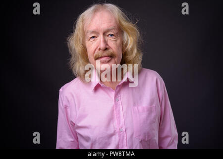 Senior businessman wearing pink shirt contre l'arrière-plan gris Banque D'Images