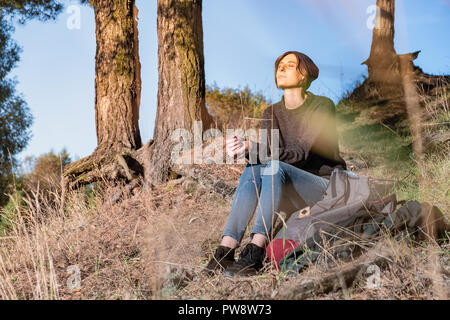 Jeune femme bénéficie d'une météo d'automne. Female hiker est assis sous les pins sur un après-midi ensoleillé Banque D'Images