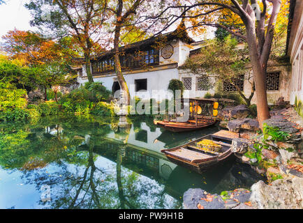 Traditionnel historique jardin botanique en ville chinoise Suzhou vue de l'intérieur de l'architecture autour de l'étang toujours avec des bateaux et des arbres. Banque D'Images