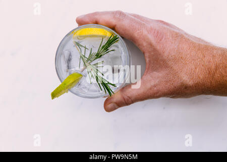 Main tenant le verre de gin tonic avec de la glace et de la chaux sur fond blanc Banque D'Images