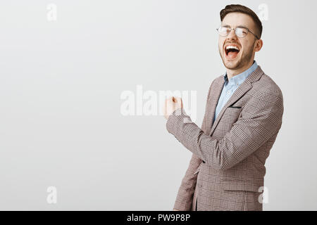 Emotive optimiste d'encouragement de l'employeur des travailleurs. Beau heureux homme de race blanche en veste et verres de crier victoire et joie sensibilisation fist dans la victoire ou la réussite sur mur gris Banque D'Images