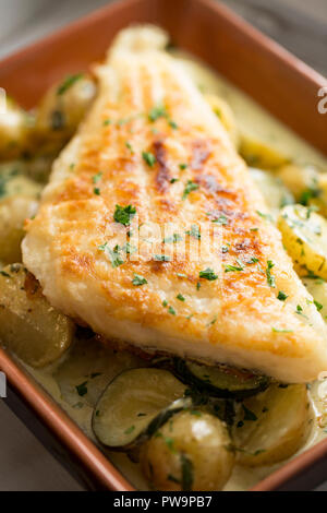 Un filet de lieu jaune, Pollachius pollachius, qui a été trempé dans la farine et frire. Il est servi sur un lit de pommes de terre bouillies, courgettes frites avec lemo Banque D'Images