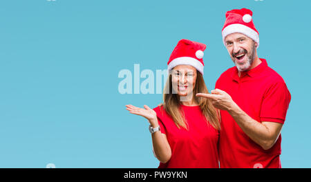 L'âge moyen hispanic couple wearing christmas hat sur fond isolé surpris et souriant à la caméra tout en se présentant avec la main et l'esprit de pointage Banque D'Images