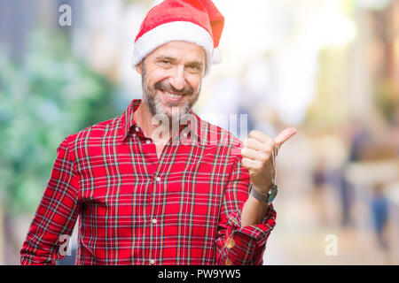 L'âge moyen le senior man wearing christmas hat sur fond isolé avec sourire heureux face à la recherche et en pointant sur le côté avec le pouce vers le haut. Banque D'Images