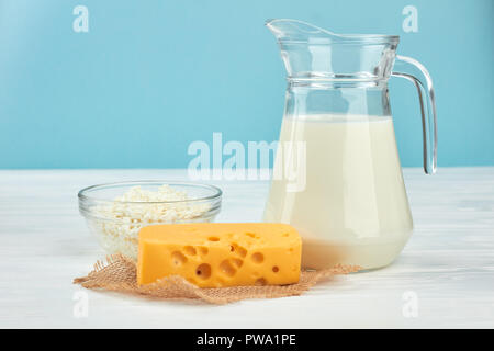 Produits laitiers sur fond bleu. Verseuse en verre dans le lait, le fromage cottage et le fromage Maasdam. Lait délicieux aliments. Banque D'Images