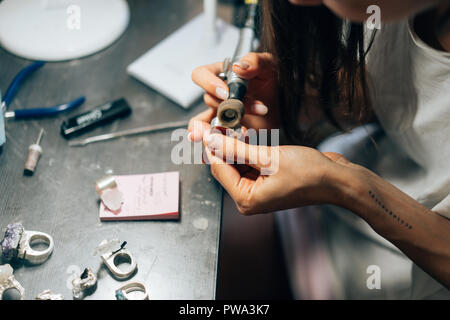 La fille travaille sur un bijoux dans l'atelier. Atelier de réparation de bijoux. Des outils, de l'argenterie et inachevé des pierres brutes. La fille est un maître joaillier. Banque D'Images