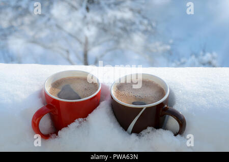 La vapeur chaude du café dans deux tasses, enterré dans la neige, sur un balcon, par un beau matin d'hiver. Le petit-déjeuner pour deux. Concept d'hiver douillet. Banque D'Images