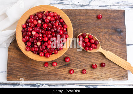 Fruits rouges mûrs d'airelles rouges dans un bol en bois sur un tableau blanc, vue du dessus Banque D'Images