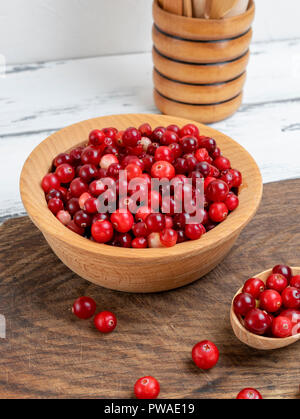 Fruits rouges mûrs d'airelles rouges dans un bol en bois sur un tableau blanc, Close up Banque D'Images