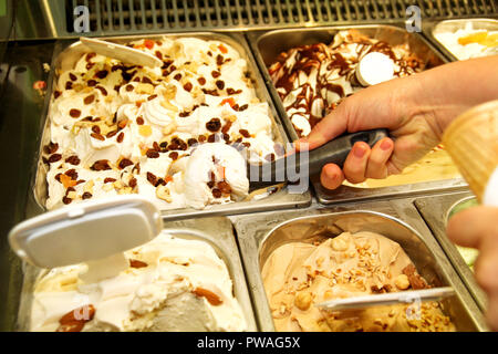 La main féminine avec boule de crème glacée dure du réfrigérateur et servir en cornet gaufré. Femme qui écope de la crème glacée savoureuse. Réfrigérateur avec de la glace. Banque D'Images