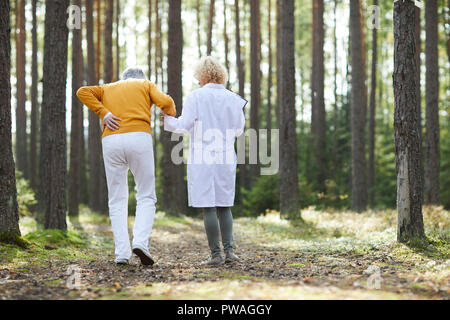 Vue arrière de doctor man avec douleur à l'arrière tout en se déplaçant vers le bas chemin forestier vers la cabine d'ambulance Banque D'Images