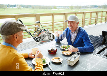 Deux joueurs de golf mature assis par table en face l'un de l'autre, avoir la salade et plateau et discuter du dernier match Banque D'Images