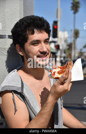 Un jeune homme appuyé contre un lampadaire de manger une tranche de pizza au pepperoni Banque D'Images