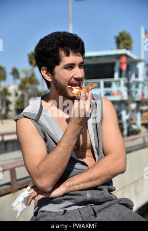 Une multi-ethnique heureux jeune homme mangeant une tranche de pizza sur la jetée par un sauveteur hut Banque D'Images