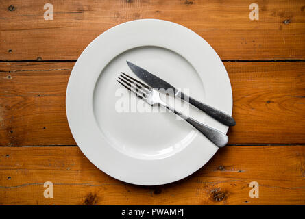 Vue de dessus d'argent fourchette et couteau sur la plaque ronde en bois blanc sur la table faisant référence que le dîner est terminé Banque D'Images