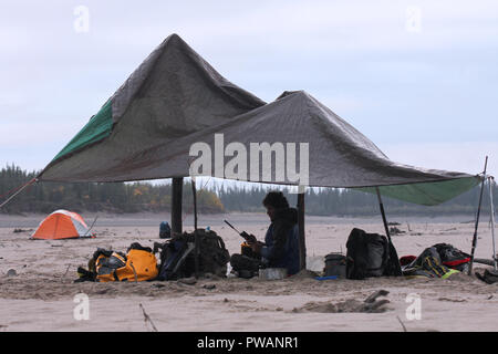 Fleuve Yukon, Territoire du Yukon, en Alaska. Vue générale du camp de l'expédition nuit sous la pluie avec un explorateur de la tentative de connexion avec un téléphone satellite. Banque D'Images