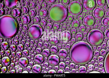 Résumé Les gouttelettes d'huile / bulles dans l'eau allumé par le bas sur un fond coloré Banque D'Images