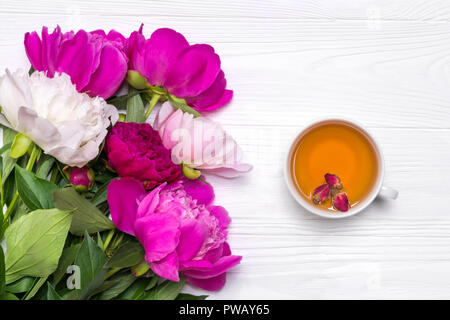 Une tasse de thé et de pivoines fleurs sur un fond en bois blanc. Immersive pour votre conception. Vue de dessus. Banque D'Images