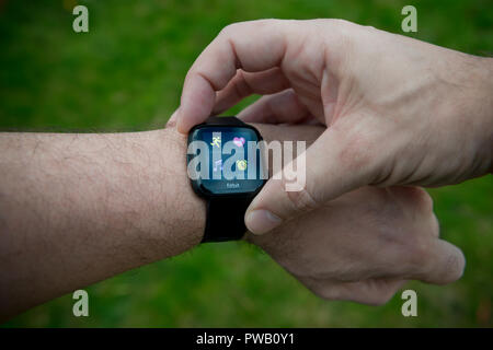 Un hommes vérifie son activité tracker Fitbit Versa y compris moniteur de fréquence cardiaque à l'aide d'unités BPM au cours d'un exercice d'entraînement. Banque D'Images