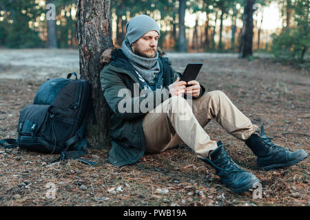 Beau mâle adultes voyageur avec sac à dos se trouve sur l'automne forêt de pins près de l'arbre, la tenue à destination de voyage de repos Loisirs Tablette Concept Banque D'Images